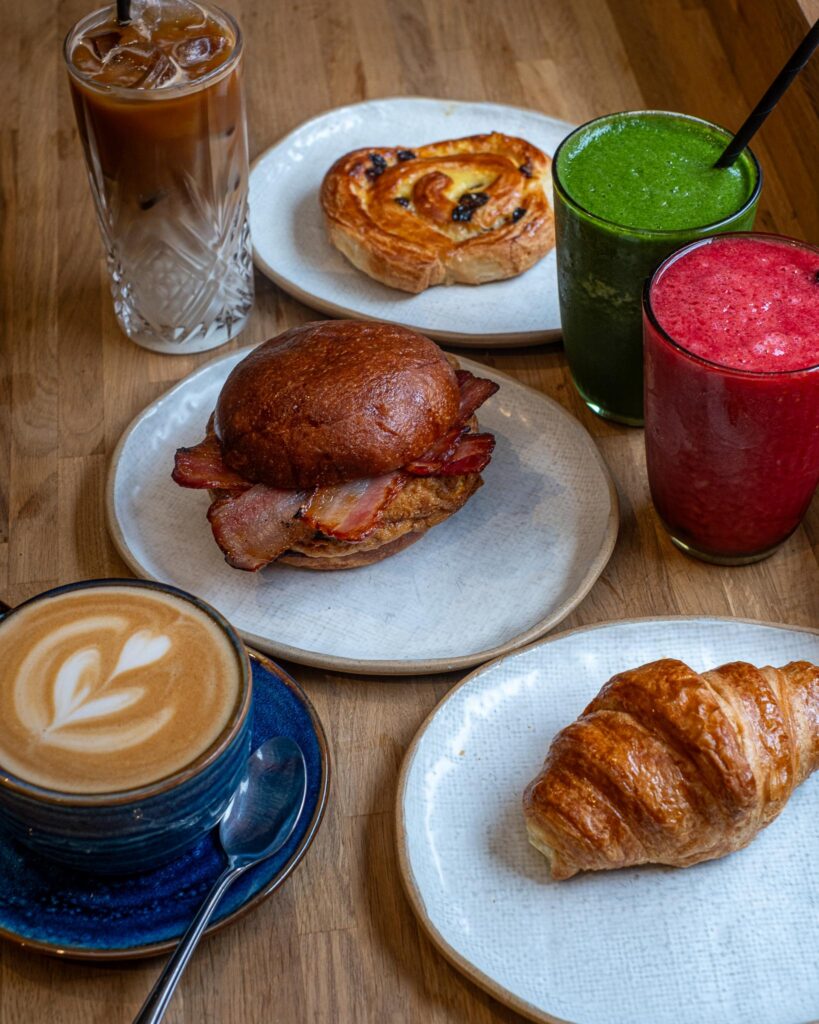 A croissant, a pastry, a bacon breakfast bun, fresh juices and coffees on a table at The Granary
