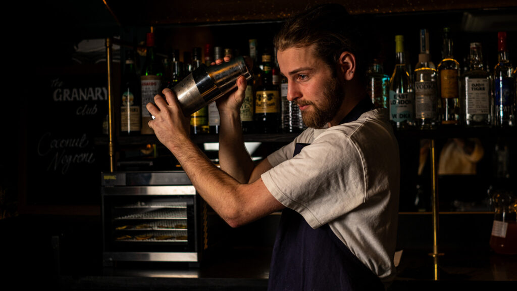 A bartender shaking a cocktail behind the bar in The Granary Club