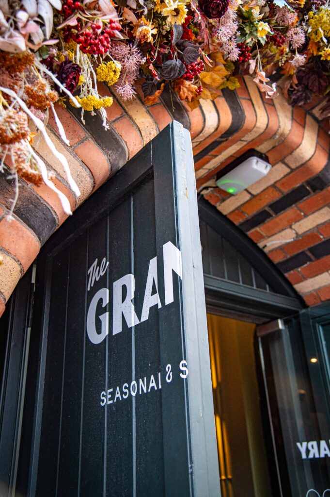 The open front door of The Granary, painted dark green with the restaurant's name, beneath a brick arch decorated with dried flowers