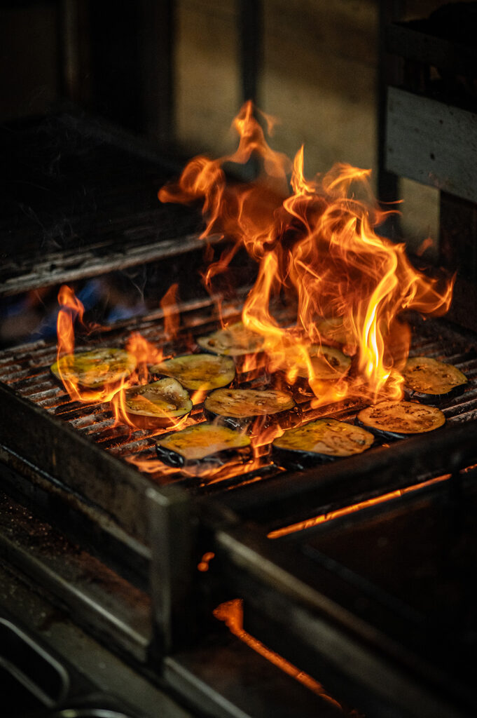 Slices of aubergine charring over open flames on the grill in The Granary kitchen