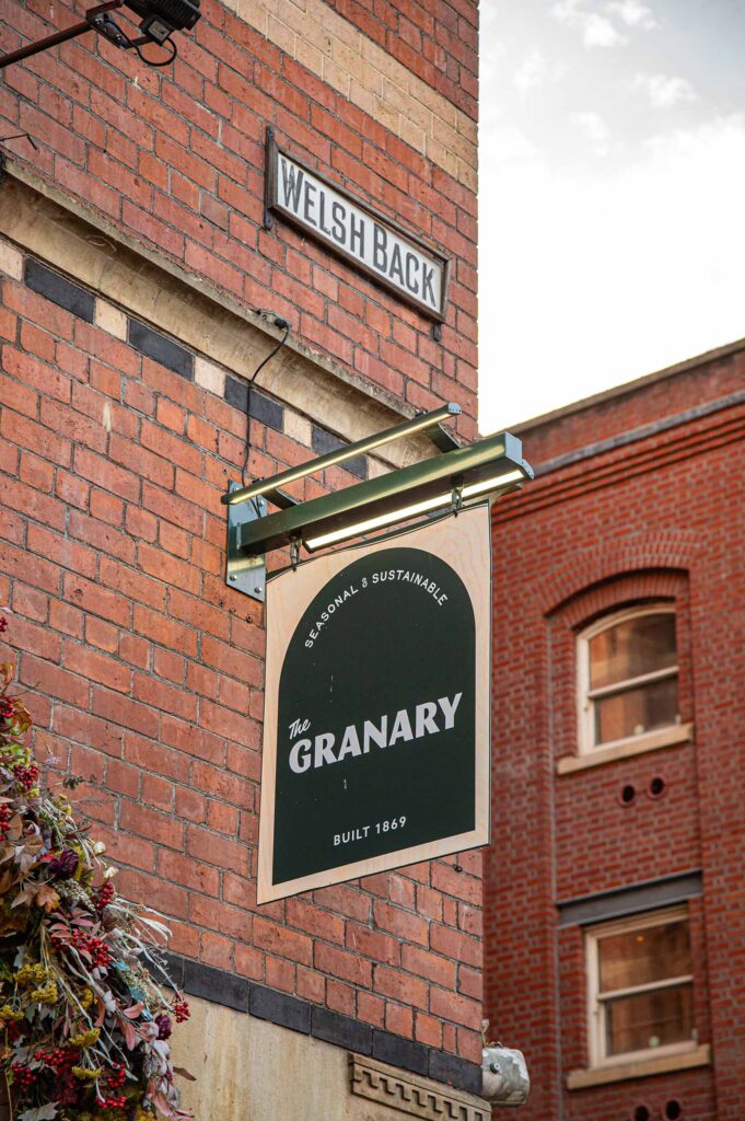 The Welsh Back street sign above The Granary's dark green hanging sign, reading "The Granary, Built 1869", on the red brick corner of the building