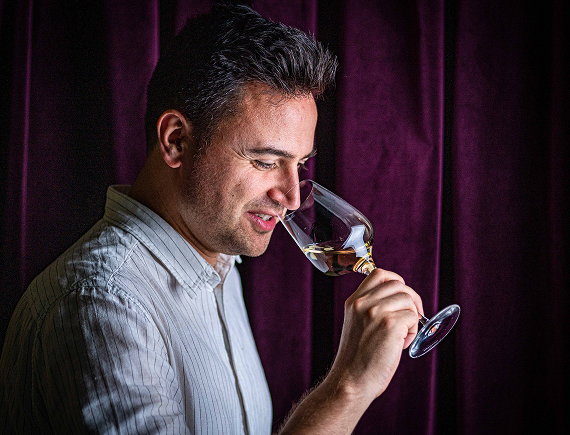A man nosing a glass of wine in front of a dark velvet curtain