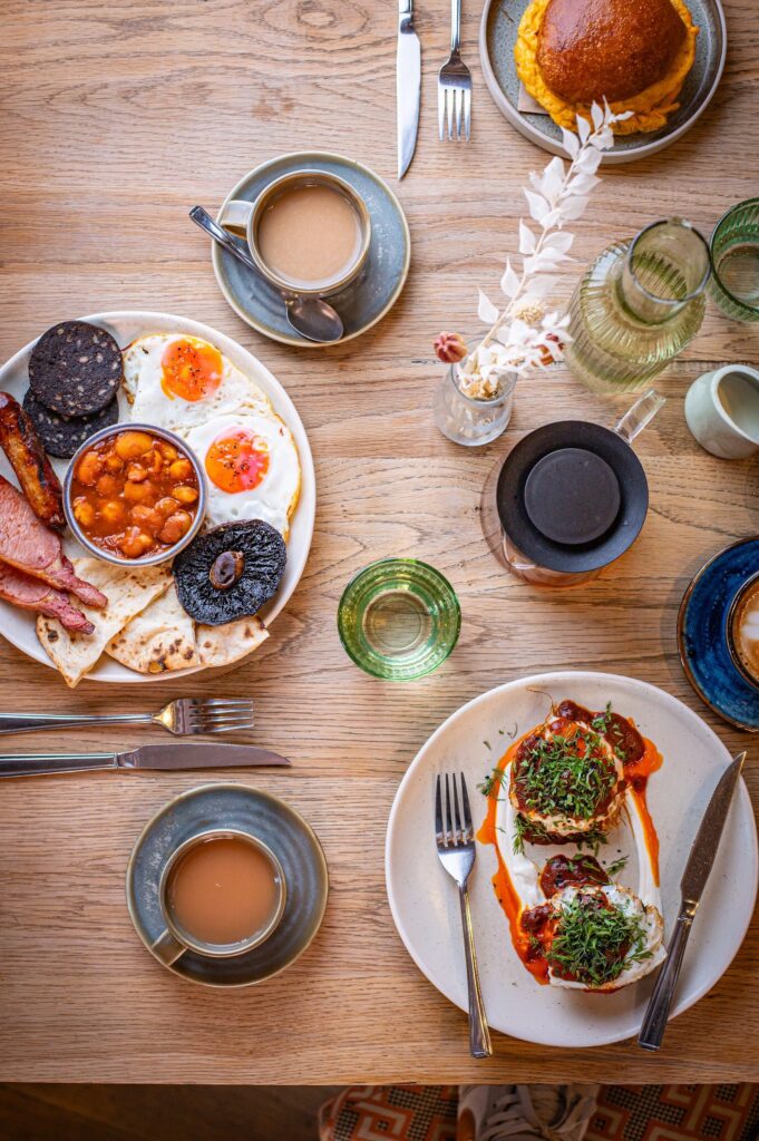 A breakfast table at The Granary seen from above, with The Granary Breakfast, Maakouda potato cakes, a breakfast bun and cups of coffee and tea