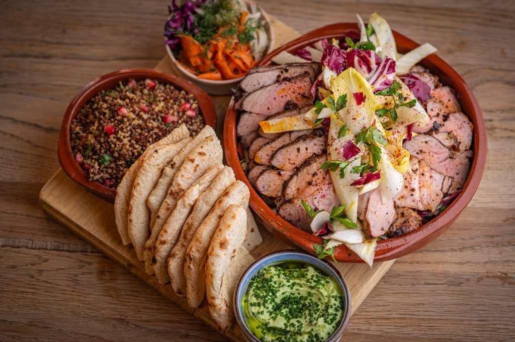 A sharing dish of sliced lamb with flatbreads, grains with pomegranate, spiced carrots and a herb dip at The Granary