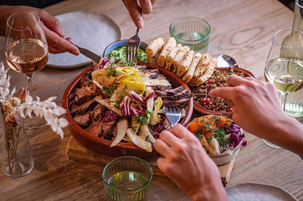 Guests sharing a dish of sliced lamb with flatbreads, grains with pomegranate and salads at The Granary