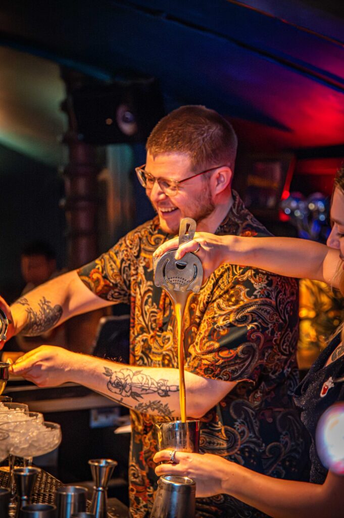 A bartender in a patterned shirt pouring a cocktail at the bar in The Granary Club