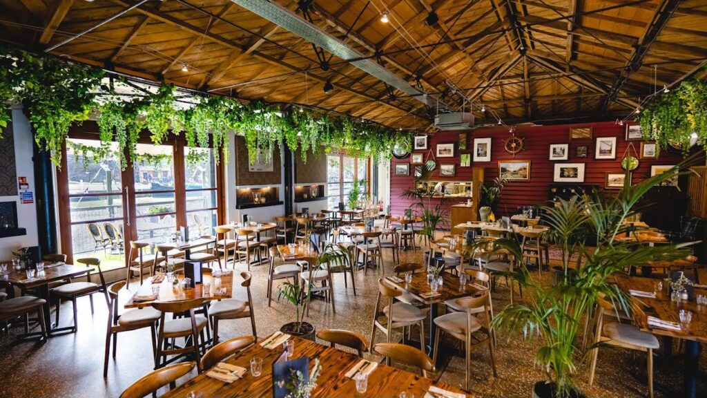 The dining room at Harbour House in Bristol, with wooden roof beams, hanging plants and laid tables