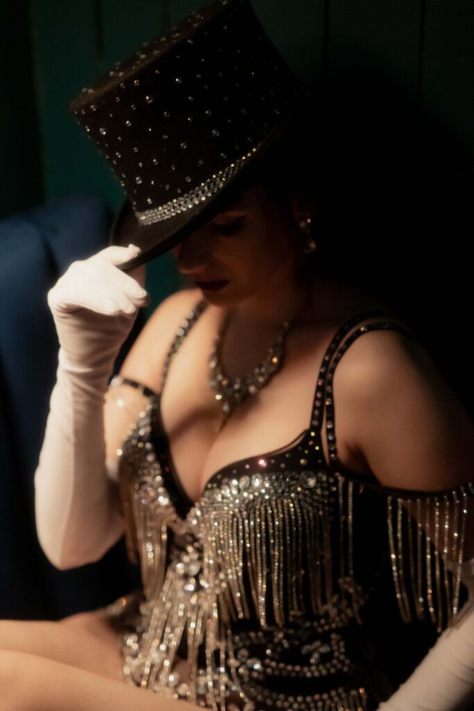 A burlesque performer tipping a jewelled top hat, in long white gloves and a crystal-fringed costume